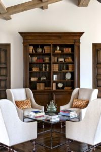 Tall dark wood book cabinet with glass doors with neutral armchairs.
