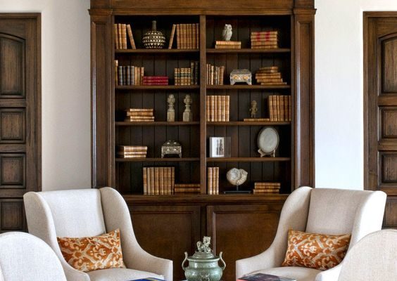 Tall dark wood book cabinet with glass doors with neutral armchairs.