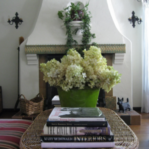 Vintage tile and plaster fireplace with vintage iron sconces, wicker table, flowers and design books.