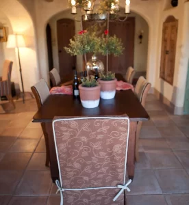 Rustic dining room table of Tua wood, matching Tua side chairs with raffia seating and slipcovered end chairs in a Spanish Craftsman  style home. Shiree Segerstrom Interior Design.