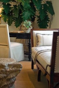 Day bed with natural fabrics, armless chair and small table furnish a corner of a room.