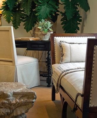 Day bed with natural fabrics, armless chair and small table furnish a corner of a room.
