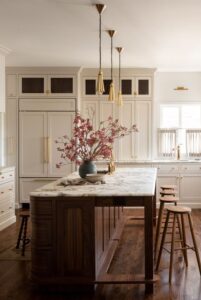 Kitchen renovated with white cabinets, gold toned lighting and pulls and marble topped island.