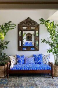 Indonesian daybed and mirror flanked by fishtail palms in baskets. Beautiful blue print fabric pillows and cushion.